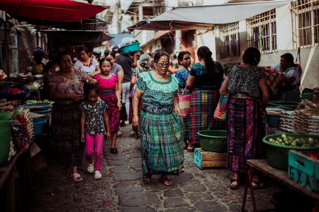 Services Women and children in colorful traditional dresses at a bustling Guatemalan market.